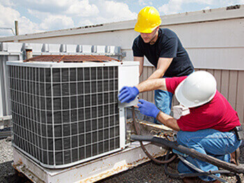 Two men in safety hats servicing an exterior HVAC unit