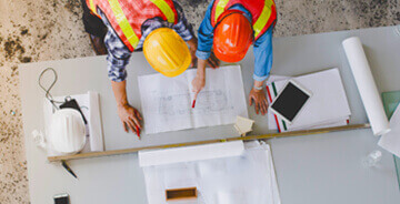 Two workers wearing construction safety hats looking at blue prints